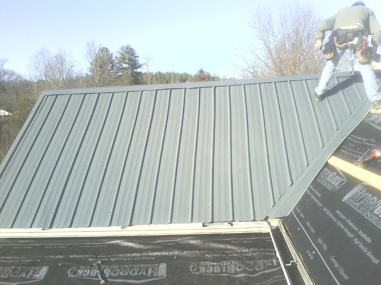 Crew installing dark green standing seam panels over synthetic underlayment in Fairfax