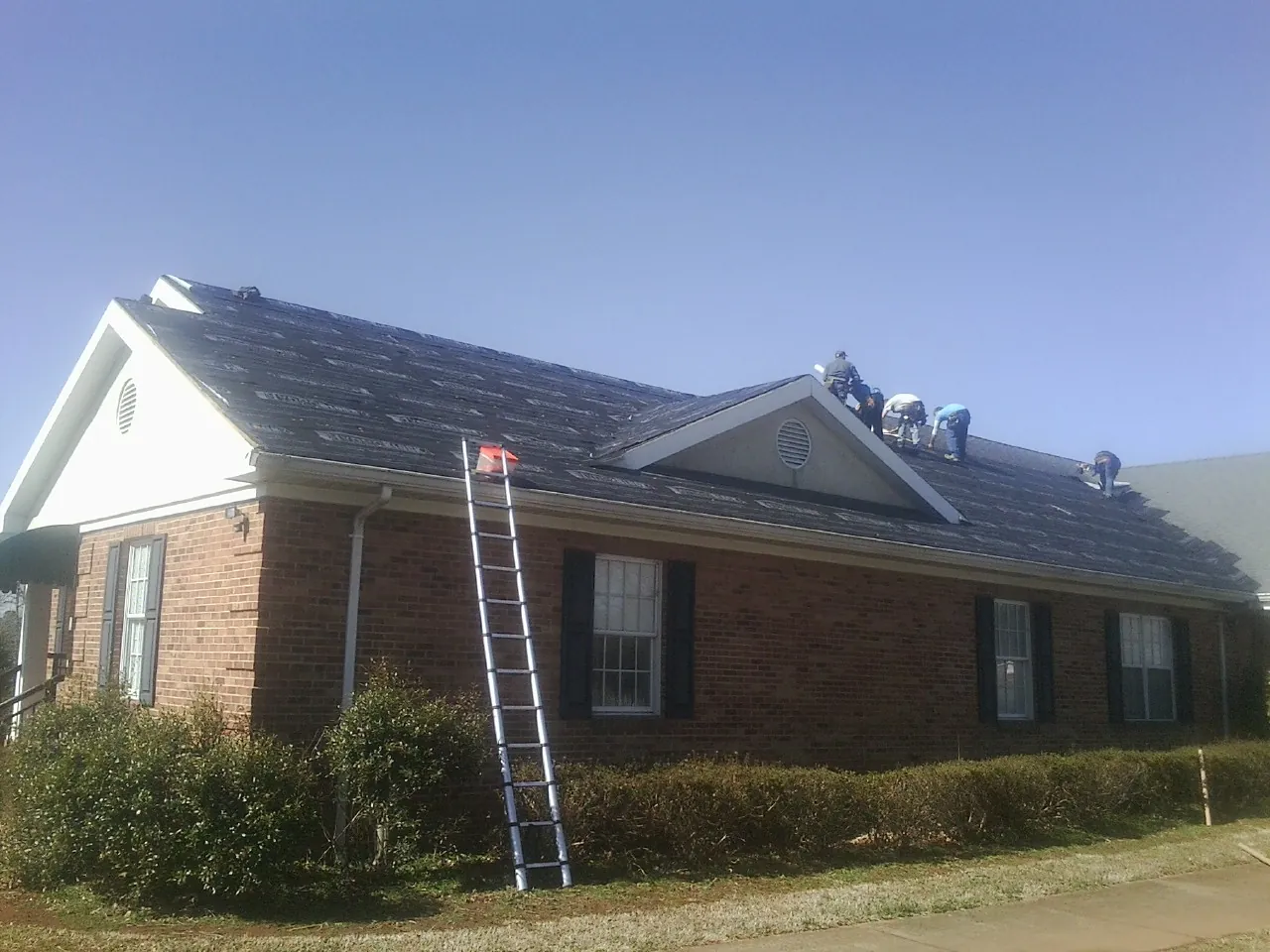 Crew tearing shingles off a brick ranch roof with a ladder set — Emergency Roof Repair work by our crew in Fairfax